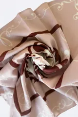 Pañuelo cuadrado tipo bandana con estampado de líneas curvas y formas abstractas en tonos marrón y crudo sobre fondo rosa.