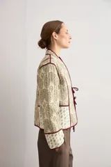 Chaqueta corta capitoneada de color verde claro con estampado tipo paisley y detalles de ribetes en color bordó. Tiene mangas largas, cuello mao y cierre frontal con lazos de atar.