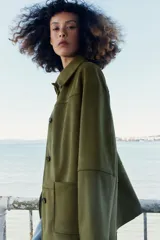 Abrigo de ante sintético color verde militar, con cuello solapa, manga larga, bolsillos delanteros de parche y cierre frontal con botones oscuros.
