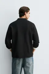 Polo de punto de manga larga con cuello solapa y cierre frontal de botones. Presenta un diseño de corte regular con aberturas laterales en el bajo.