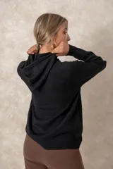 Buzo de punto negro con capucha, cordones ajustables con terminales metálicos, mangas raglán y bolsillo tipo canguro frontal.