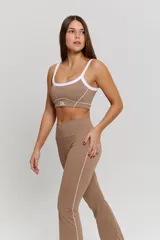 Conjunto deportivo compuesto por un top y un pantalón largo color habano. El top es de escote redondo con breteles blancos y detalle de logo 'bk.' en el frente. El pantalón es de tiro alto con costuras laterales blancas y corte ligeramente acampanado en el ruedo.
