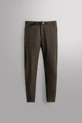 Pantalón largo color verde oscuro, de corte slim fit y tiro medio. Confeccionado en tejido técnico elástico, con cintura ajustable mediante cinturón con hebilla plástica. Presenta bolsillos laterales con cierre de cremallera oculta y bolsillo trasero con cierre de cremallera oculta.