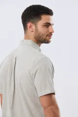 Camisa de manga corta confeccionada en mezcla de lino y algodón, con estampado de cuadros pequeños en tonos azules. Presenta cuello camisero con botones, cierre frontal abotonado, bolsillo aplicado en el pecho y dobladillo redondeado.