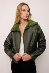 Chaqueta estilo bomber de cuero vacuno en color verde vintage, con cuello y forro interior de corderito al tono. Presenta cierre frontal completo y un diseño de inspiración retro con acabado texturizado.