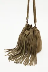 Cartera tipo bucket bag de cuero vacuno color verde oliva, con diseño de flecos largos y detalles de tachas metálicas. Cuenta con cierre de cordón ajustable y correa larga para llevar al hombro o cruzada.