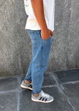 Pantalón de jean estilo slouchy en color azul medio, con corte holgado en la parte superior y ajuste hacia los tobillos, con ruedo doblado.
