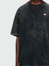 Remera Diesel de corte oversize con efecto lavado ácido en tonos oscuros. Presenta cuello redondo y un pequeño parche rectangular con el logo de la marca en el pecho.