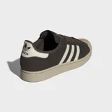 Championes Adidas Superstar II de cuero nobuk en color marrón oscuro, con las icónicas tres rayas laterales y la puntera de caucho en tono crema. Presenta una suela de caucho al tono y forro interior de felpa.