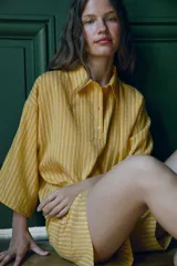 Camisa de corte holgado confeccionada en mezcla de lyocell, con estampado de rayas verticales en tonos amarillos y blancos. Presenta cuello solapa, cierre frontal parcial con botones y mangas anchas por debajo del codo.