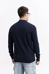 Campera tejida de algodón en color beige, con cierre frontal completo, cuello levemente elevado y puños y ruedo acanalados. Presenta un pequeño logo bordado en el pecho.