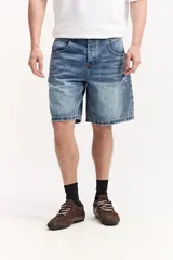 Bermuda de jean de corte amplio y largo hasta la rodilla, en tono azul con lavado desgastado y detalles de roturas sutiles.