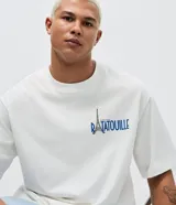 Remera de corte boxy color blanco, con cuello redondo y manga corta. Presenta un estampado artístico en la espalda con diversos personajes y elementos de la película Ratatouille.