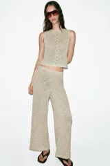 Top tipo chaleco de tejido de punto con algodón, color beige con detalles texturizados. Presenta cuello redondo, sin mangas y cierre frontal con una hilera de botones.