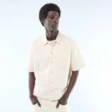Camisa vaquera de manga corta en color beige, con cuello clásico, cierre frontal de botones y un bolsillo aplicado en el pecho.