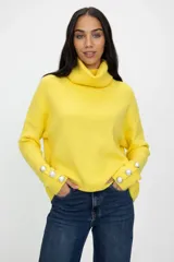 Polerón de cuello alto en color amarillo, con mangas largas y detalle de botones decorativos en los puños.