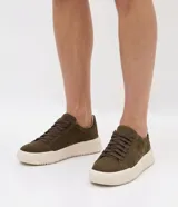 Championes casuales de color verde militar, confeccionados en material sintético con acabado liso, diseño de corte bajo, cordones al tono y suela chunky de goma en color off-white.