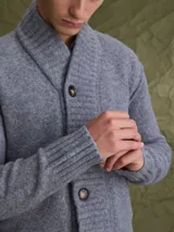 Cardigan de punto gris con cuello tipo chal y cierre frontal de botones. Presenta puños y ruedo acanalados, ofreciendo un diseño clásico y versátil.