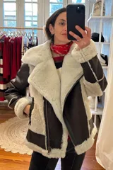 Campera tipo gamulán de cuero genuino color marrón oscuro, con interior y detalles en piel sintética color crema. Presenta cierre frontal cruzado, bolsillos laterales con cierre y puños con borde de piel.