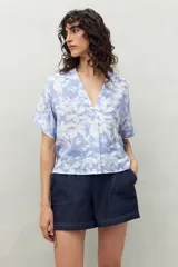 Camisa de manga corta con estampado de hojas blancas sobre fondo celeste, cuello solapa y botones de nácar al frente.