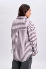 Camisa de manga larga con diseño de rayas verticales en tonos violeta y blanco, corte oversize, cuello camisero, cierre frontal con botones y detalles de lazos en el frente.