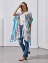 Kimono ligero de manga corta, color blanco, con estampado floral estilo cachemira en tonos pastel (naranja, verde menta, celeste). Presenta bordes y detalles en azul turquesa con borlas colgantes en el ruedo.