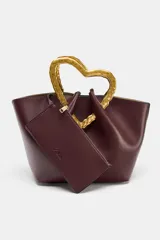 Bolso de mano tipo saco, color borgoña, con asa superior metálica con forma de corazón martillado en tono dorado. Incluye un compartimento interior extraíble y cierre mediante botón metálico.