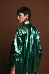 Camisa verde metalizada de corte holgado, con cuello clásico, cierre frontal con botones y mangas largas.