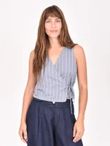 Chaleco cruzado sin mangas de color azul con finas rayas verticales blancas, diseño con escote en V y ajuste lateral mediante lazo.