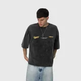 Remera de corte oversize con efecto acid wash en color gris oscuro. Presenta estampado gráfico en color amarillo en el frente con el logo de la marca y detalles de texto.
