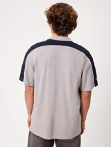 Remera polo gris melange de ajuste holgado, con cuello y cierre frontal de botones. Presenta detalles en azul marino y blanco en los hombros y mangas, y el logo de la marca bordado en el pecho.