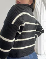 Sweater de punto grueso negro con rayas horizontales blancas, cuello alto y corte holgado.