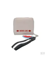 Billetera tipo monedero de cuero sintético negro con parche frontal blanco que incluye el texto 'MON AMOUR' y logo de la marca. Incluye una correa de muñeca a rayas y un dije colgante en forma de labios rojos.