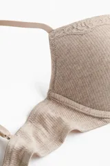 Soutien push-up color beige en punto acanalado, con copas acolchadas, aros, breteles ajustables y cierre de corchetes en la espalda. Presenta detalles de encaje en la parte superior de las copas y un pequeño lazo en el centro.