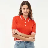 Sweater de punto canalé color naranja, de manga corta, con cuello polo blanco y ribetes a rayas blancas en el cuello, puños y dobladillo. Presenta cierre frontal con botones dorados.