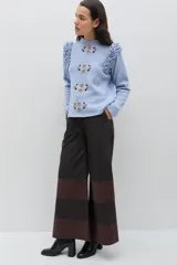 Pantalón de corte amplio y pierna ancha, confeccionado en gabardina de algodón con acabado engomado. Presenta un diseño de paneles horizontales en contraste de colores marrón y negro, con cierre frontal y bolsillos laterales.