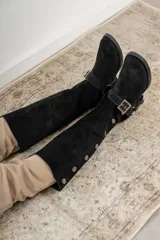 Botas altas de gamuza negra con hebilla y botones dorados.