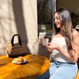 Cartera tipo tote de cuero color beige, con doble asa corta marrón y cierre superior con cremallera. Tiene un bolsillo frontal con cremallera y forro interior de tela con un bolsillo.