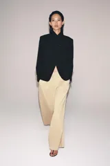 Pantalón de tiro medio con corte wide leg, confeccionado en algodón. Presenta cintura con trabillas, bolsillos laterales ocultos y detalle de pliegues en el delantero. Cierre frontal con cremallera, botón y ganchos metálicos.