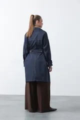 Trench de diseño clásico en color beige, con cierre frontal de botones, cinturón ajustable con hebilla a tono y mangas con trabillas en los puños.