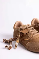 Zapatillas urbanas de gamuza color marrón, con diseño de cordones decorados con cuentas de piedra y detalles de líneas brillantes en los laterales. Presentan suela de goma texturizada al tono.