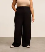 Pantalón negro de vestir, tiro alto, corte wide leg (pierna ancha), con bolsillos laterales y cierre frontal con cremallera y gancho.