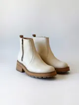 Bota corta de cuero vacuno con textura granulada, color crudo. Presenta cierre lateral metálico, suela track de goma en tono suela y tirador trasero.