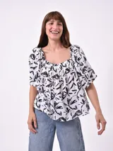 Blusa blanca con estampado abstracto en negro, escote cuadrado fruncido y mangas cortas abullonadas.