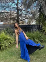 Vestido largo de satén color marrón con acabado metalizado, escote en V, tirantes finos cruzados en la espalda y diseño con corte bajo el busto y volados en la falda.