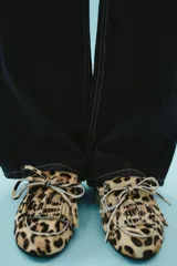 Mocasín plano de piel con pelo con estampado animal print, detalle de flecos y lazo en la parte delantera, pespuntes en contraste y punta redonda.