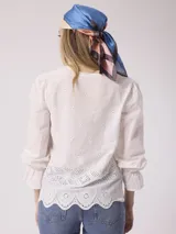 Blusa blanca de algodón con bordado calado, escote en V con lazos, mangas largas con volados en los puños y corte holgado.