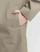 Gabardina clásica de corte recto, color beige, con cuello camisero, cierre frontal de botones y bolsillos laterales. Confeccionada en tejido técnico repelente al agua y al viento.