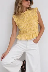 Top sin mangas con estampa a cuadros vichy en tonos amarillos y blancos, diseño fruncido con volados en los hombros y cuello alto.