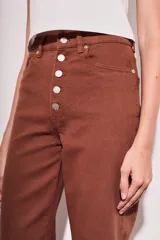 Pantalón de jean color marrón, de corte recto y tiro medio, con cierre frontal con botones.